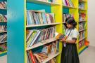 An image of a schoolgirl in uniform standing in front of a bookshelf in a school library.